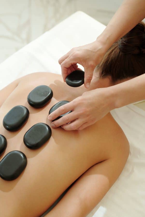 Hands of masseuse putting hot spa stones on female back